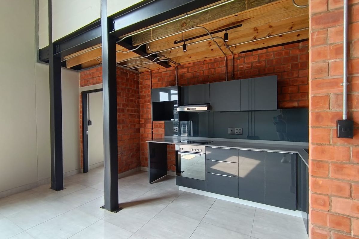 Modern industrial-style kitchen featuring exposed brick walls, steel beams, timber ceiling, and sleek grey cabinetry with integrated appliances.