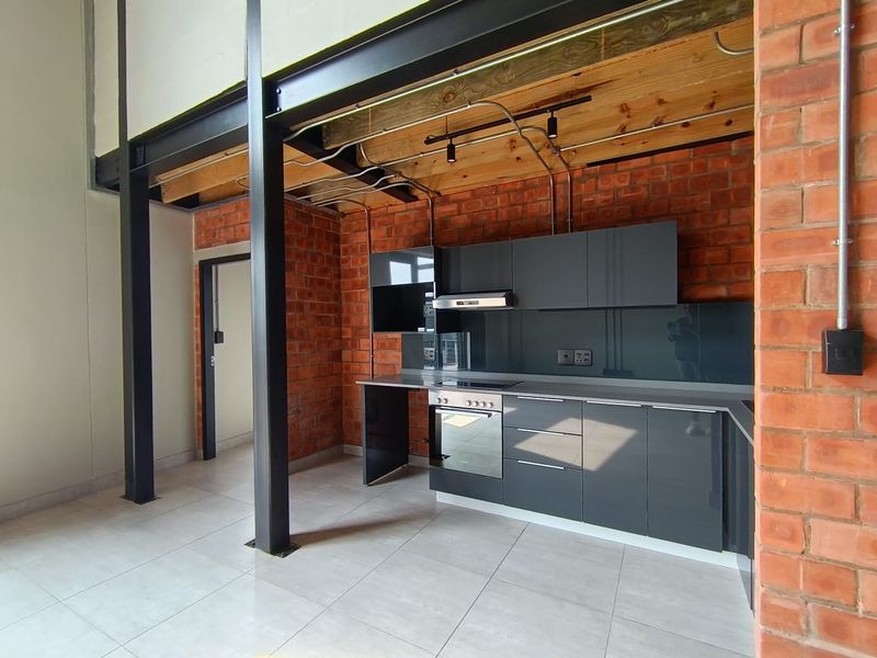 Modern industrial-style kitchen featuring exposed brick walls, steel beams, timber ceiling, and sleek grey cabinetry with integrated appliances.