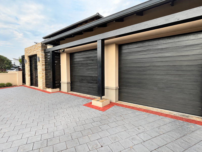 Modern double garage facade featuring dark horizontal panel doors, stone cladding accents, and a well-maintained paved driveway.
