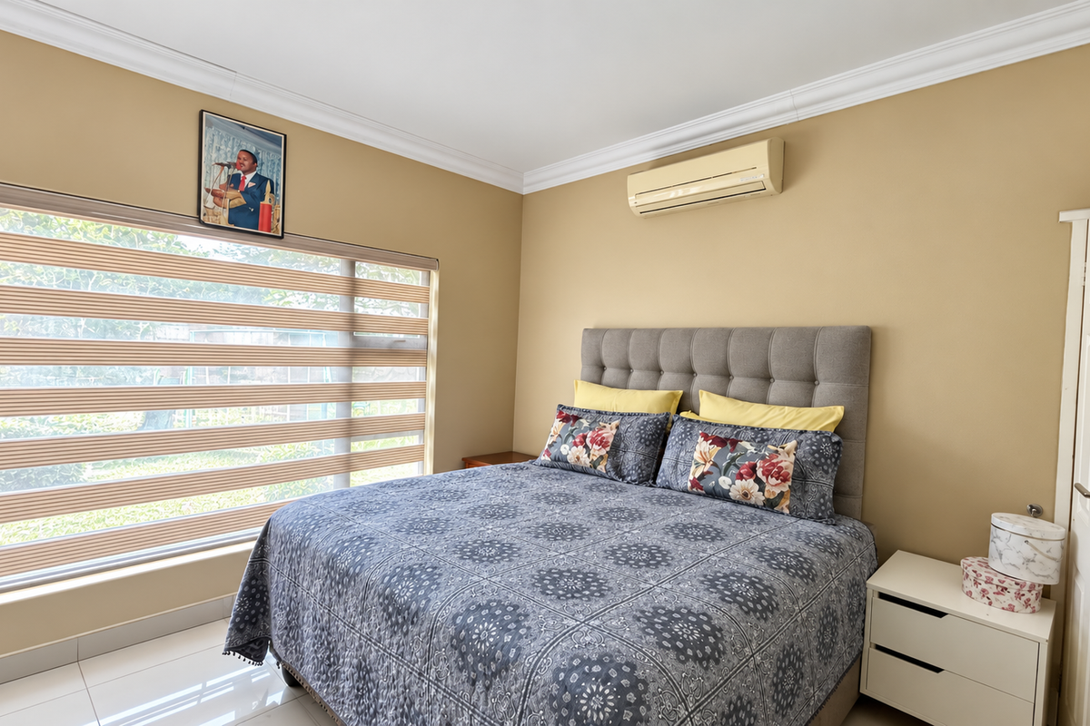 A well-maintained bedroom featuring tiled flooring, crown molding, and a wall-mounted split-system air conditioner, providing a comfortable and functional living space.