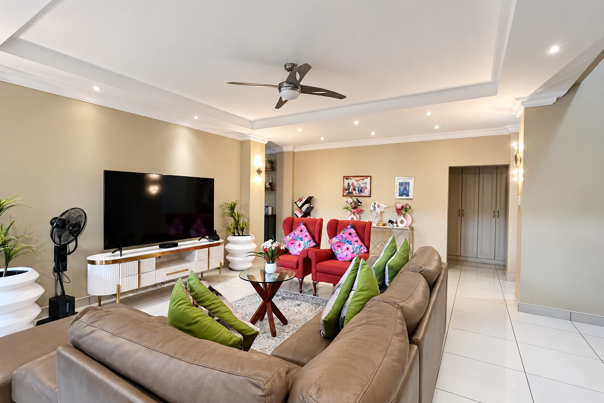 Spacious living room featuring recessed ceiling detail, modern downlighting, a ceiling fan, and polished floor tiles, leading to a built-in storage area.