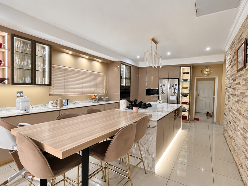 Modern kitchen featuring a large marble-look island, integrated cabinetry, stone cladding feature wall, and high-end finishes with recessed and under-cabinet lighting.