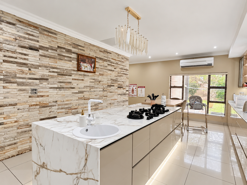 Modern kitchen featuring a large marble-look island with integrated gas hob, stone veneer feature wall, sleek cabinetry, and high-quality tiled flooring.