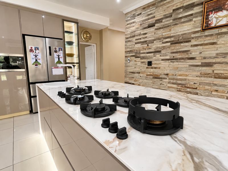 Modern kitchen featuring a large island with a built-in gas cooktop, stone countertops, high-gloss cabinetry, and a decorative stone feature wall.