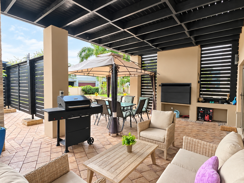 Spacious covered patio featuring a built-in braai, tiled flooring, and exposed beam ceiling, ideal for outdoor entertaining and relaxation.