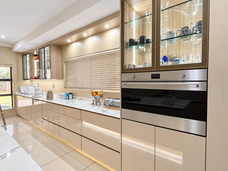 Modern, high-end kitchen featuring sleek gloss cabinetry, stone countertops, integrated oven, gas hob, and elegant glass-front display cabinets with ambient under-cabinet lighting.