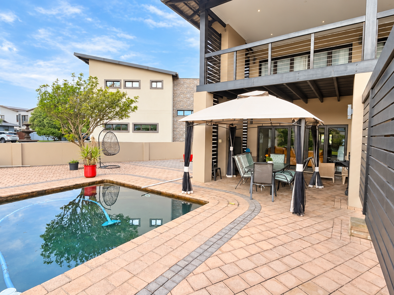 Outdoor entertainment area featuring a swimming pool, paved patio, and a covered balcony with a modern timber privacy screen.