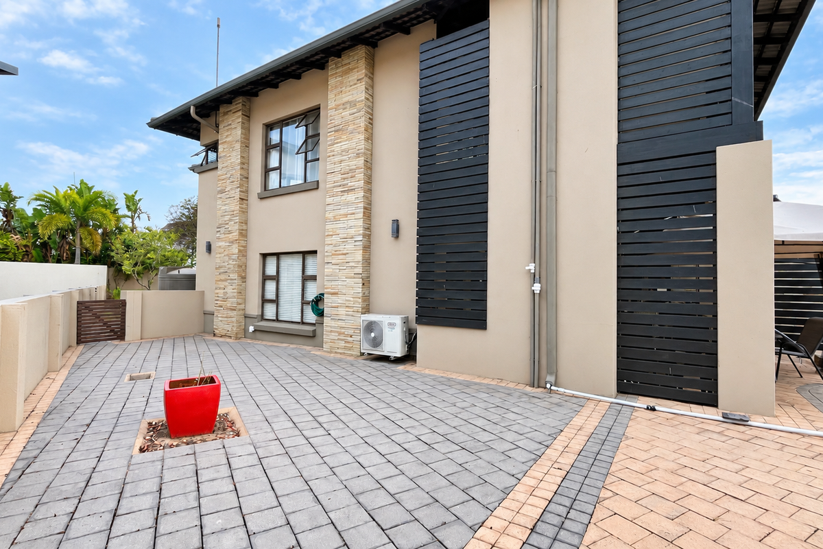 A well-maintained rear exterior featuring stone-clad pillars, modern timber privacy screens, and a spacious paved patio area.