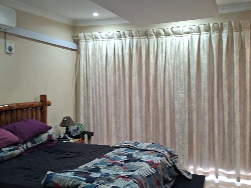 A bedroom featuring a wall-mounted split-system air conditioner, recessed ceiling detail, and full-length window curtains.