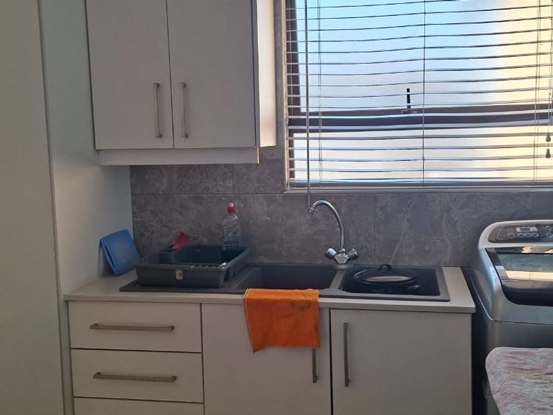 Functional laundry area featuring built-in cabinetry, a double sink with mixer tap, and tiled backsplash, providing practical utility space.