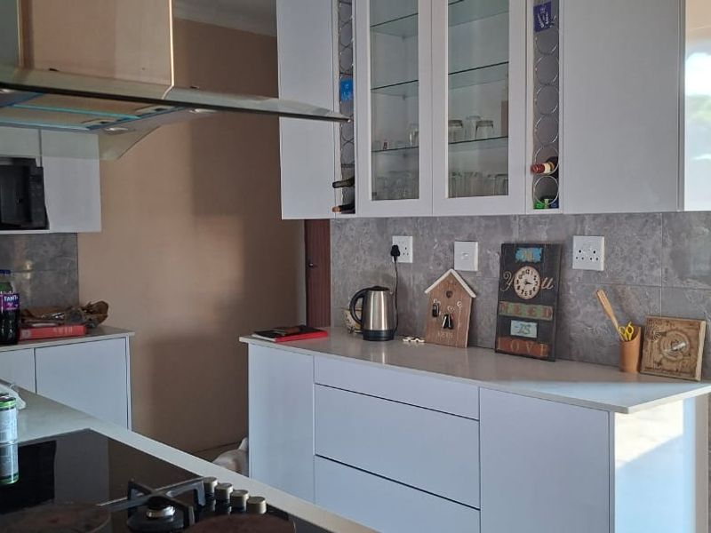 Modern kitchen featuring white cabinetry, stone countertops, tiled backsplash, built-in oven, hob, and a stainless steel extractor fan with direct access to the exterior.
