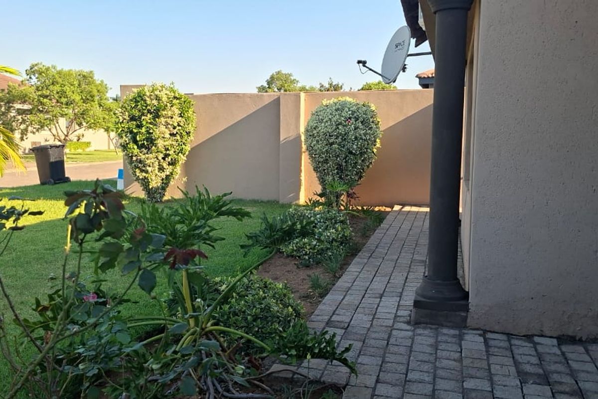 A well-maintained rear garden area featuring a paved walkway, boundary wall, and established landscaping alongside the side of the house.