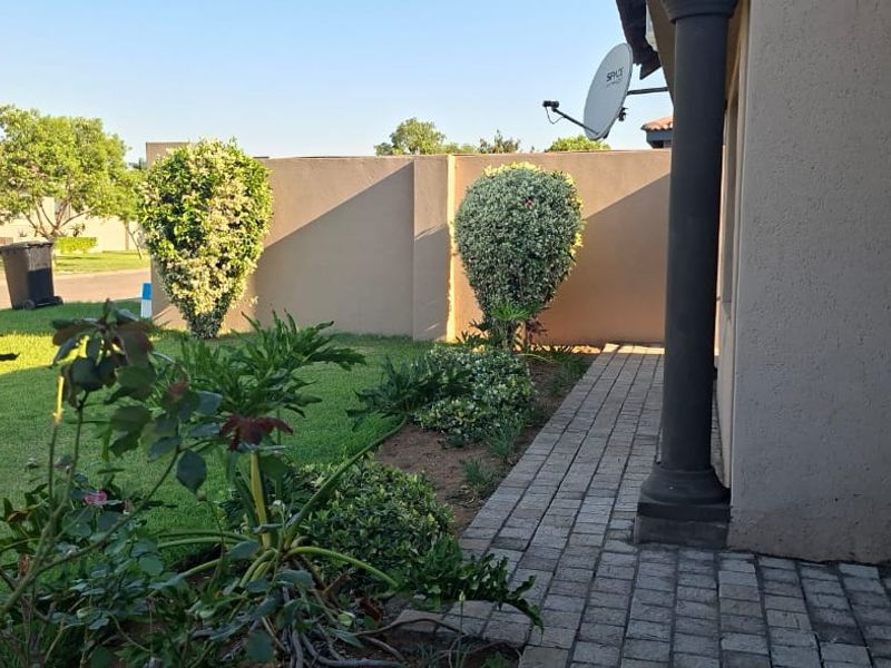 A well-maintained rear garden area featuring a paved walkway, boundary wall, and established landscaping alongside the side of the house.