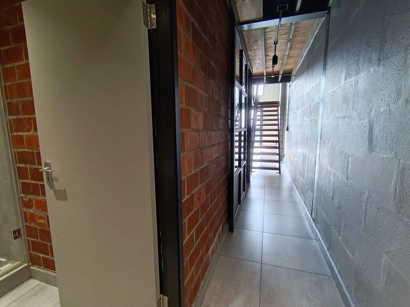 A modern industrial-style hallway featuring exposed brick and concrete block walls, tiled flooring, and a timber staircase leading to an upper level.