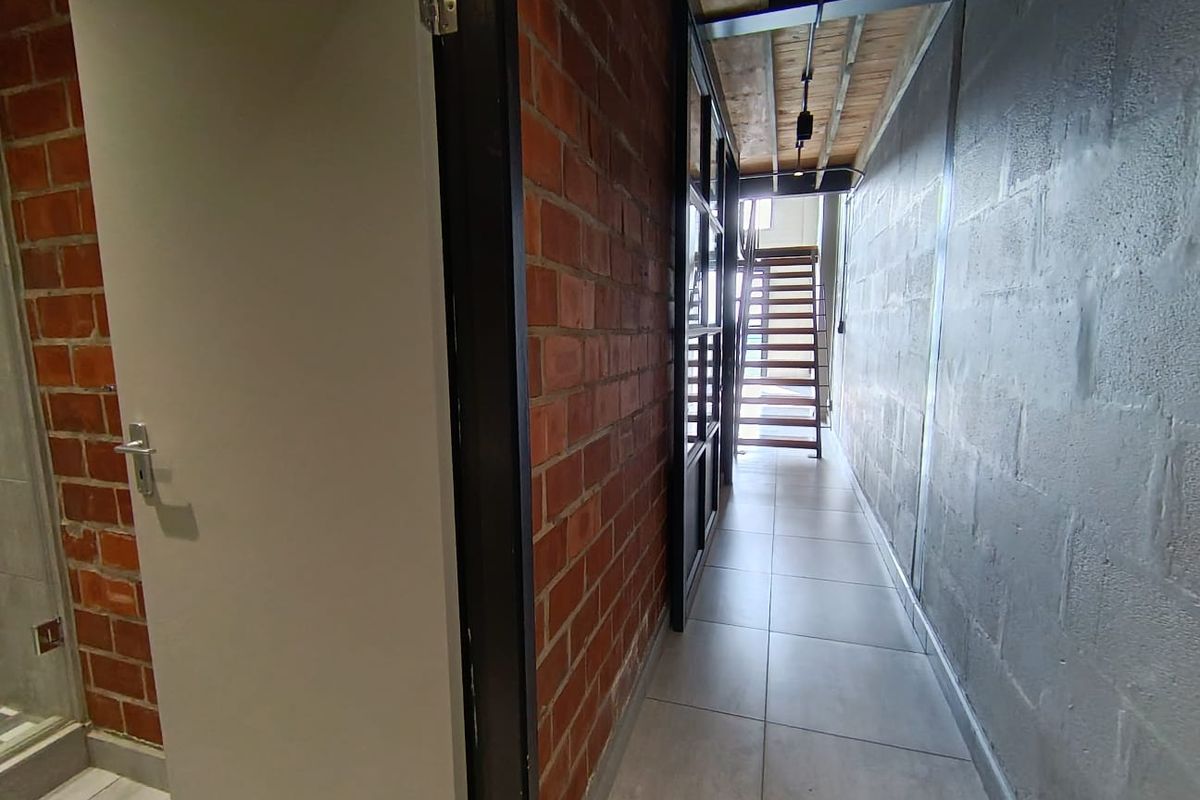 A modern industrial-style hallway featuring exposed brick and concrete block walls, tiled flooring, and a timber staircase leading to an upper level.