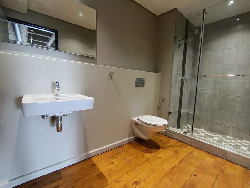 Modern bathroom featuring a wall-mounted basin, wall-hung toilet, and a glass-enclosed shower with contemporary finishes and timber flooring.