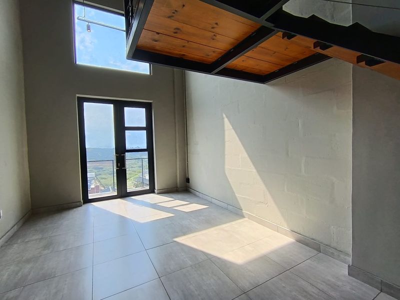 A bright, double-volume living area featuring modern tiled floors, large windows, and a striking industrial-style staircase leading to an upper level.