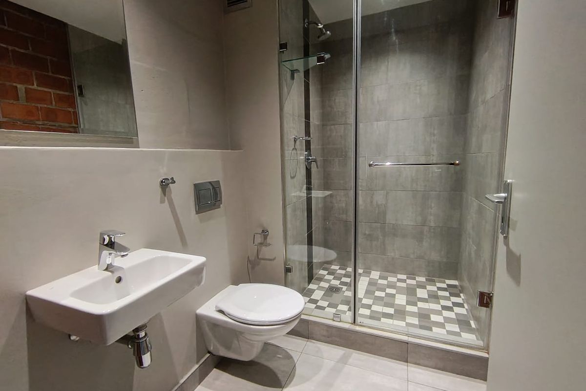 Modern bathroom featuring a wall-mounted basin, wall-hung toilet, and a glass-enclosed shower with a stylish tiled floor and exposed brick accent wall.