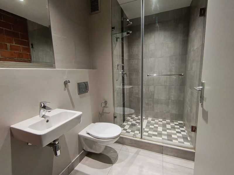 Modern bathroom featuring a wall-mounted basin, wall-hung toilet, and a glass-enclosed shower with a stylish tiled floor and exposed brick accent wall.