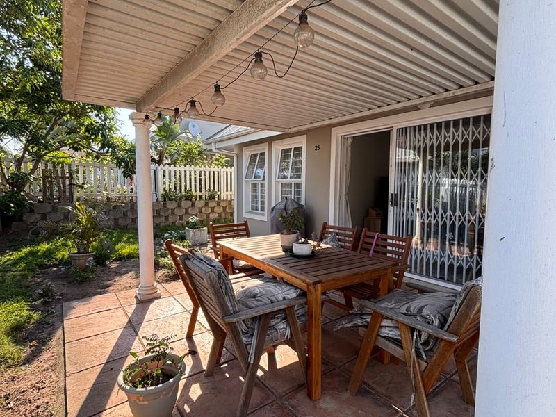 A covered outdoor patio area featuring tiled flooring, support columns, and direct access to the interior through a sliding glass door with security gate.