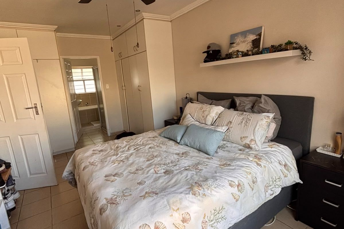 A bedroom featuring built-in cupboards, a ceiling fan, and tiled flooring, with an adjoining bathroom visible through the doorway.