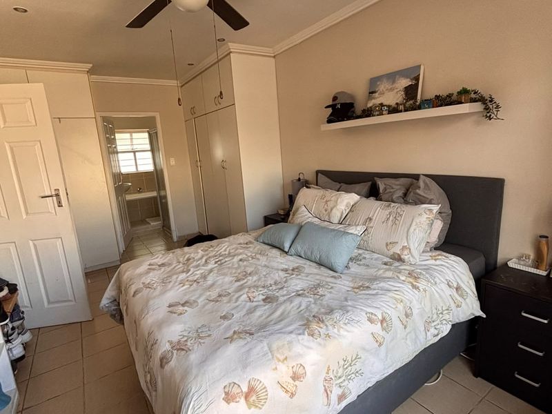 A bedroom featuring built-in cupboards, a ceiling fan, and tiled flooring, with an adjoining bathroom visible through the doorway.