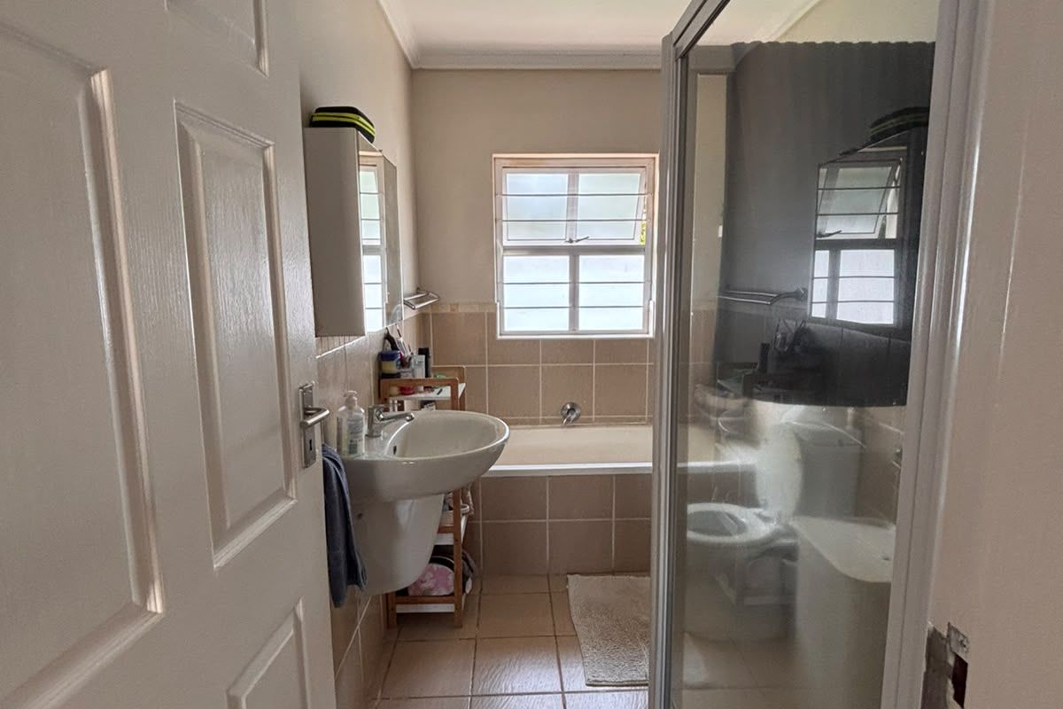A functional bathroom featuring a pedestal basin, a built-in bathtub, and a separate shower enclosure with tiled finishes throughout.