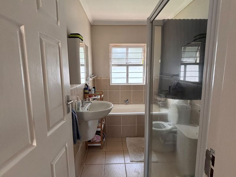 A functional bathroom featuring a pedestal basin, a built-in bathtub, and a separate shower enclosure with tiled finishes throughout.
