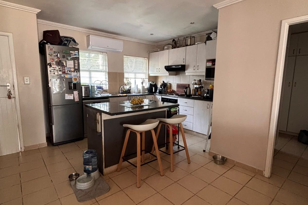 A functional kitchen featuring a central island, built-in cabinetry, and tiled flooring, equipped with an extractor fan and wall-mounted air conditioning unit.