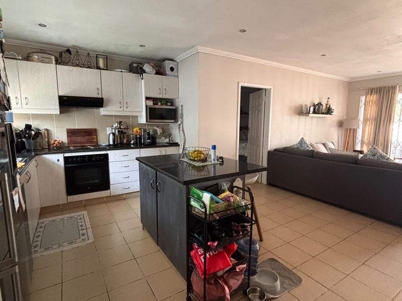 Open-plan kitchen and living area featuring a central island, built-in cabinetry, integrated appliances, and neutral tiled flooring throughout the space.