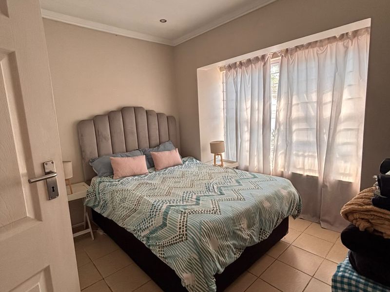 A well-maintained bedroom featuring tiled flooring, recessed downlighting, and a window with security bars, offering a comfortable and functional living space.