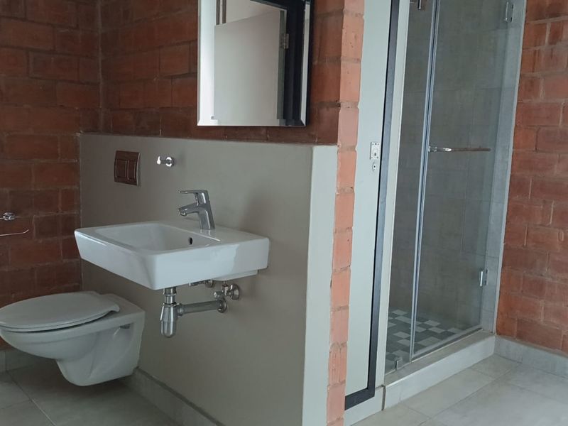 Modern bathroom featuring a wall-mounted toilet, basin, and a glass-enclosed shower, complemented by industrial-style exposed brick walls and neutral floor tiles.
