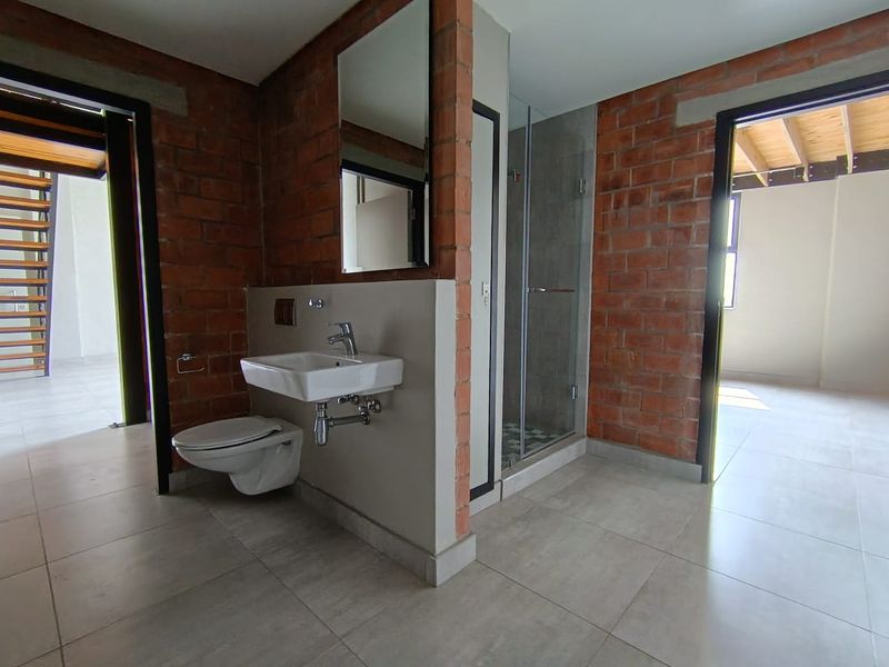 Modern bathroom featuring exposed brick walls, a wall-mounted basin, wall-hung toilet, and a glass-enclosed shower with tiled flooring.