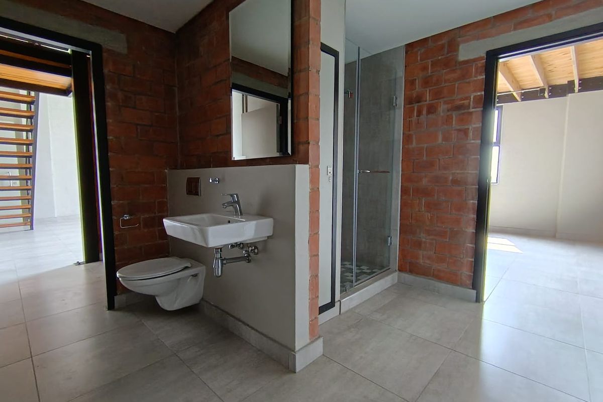 Modern bathroom featuring exposed brick walls, a wall-mounted basin, wall-hung toilet, and a glass-enclosed shower with tiled flooring.