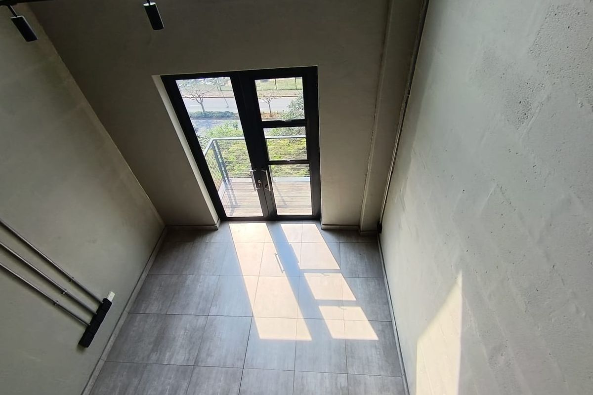A bright, double-volume living area featuring modern tiled floors, exposed blockwork walls, and double glass doors leading to an outdoor balcony.