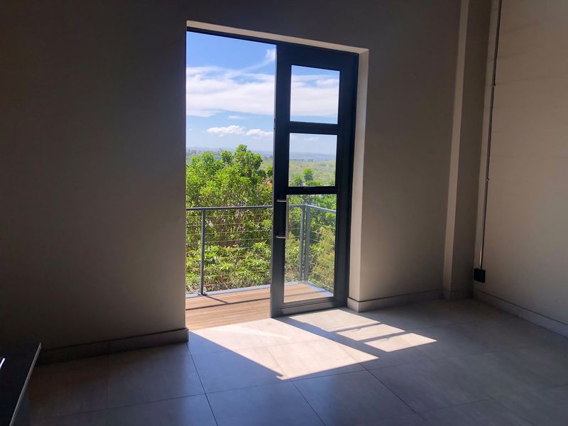 An interior view of a balcony featuring timber decking and a metal railing, accessible through a modern glass door with scenic outdoor views.