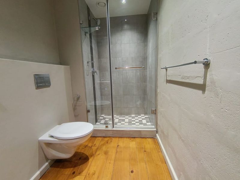 Modern bathroom featuring a wall-mounted toilet, glass-enclosed shower with tiled flooring, and warm timber flooring throughout.