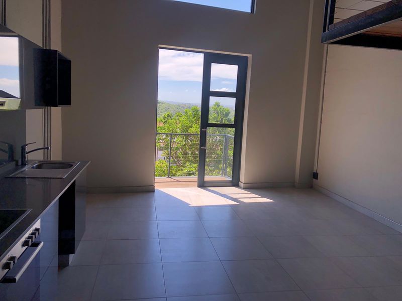 Modern open-plan apartment living area featuring a sleek kitchen, tiled floors, and direct access to a balcony with scenic views.