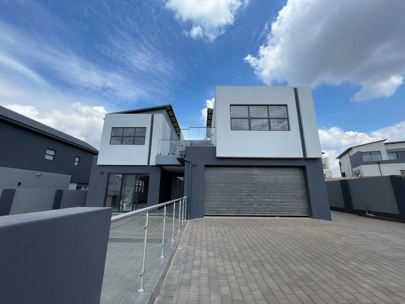 Modern double-story residential property featuring a paved driveway, integrated double garage, and a contemporary facade with glass balustrade detailing.