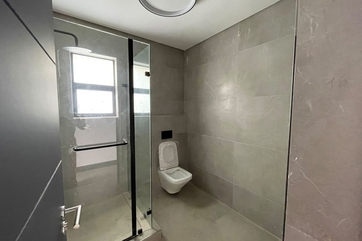 Modern bathroom featuring large format grey tiling, a glass-enclosed walk-in shower with a rain shower head, and a wall-mounted toilet.