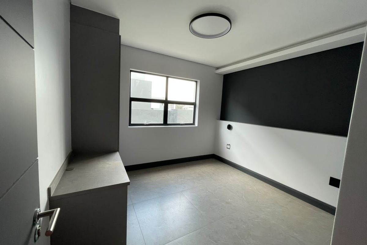 A modern, empty bedroom featuring neutral tiled flooring, built-in cabinetry, and a contemporary two-tone wall finish with large window.