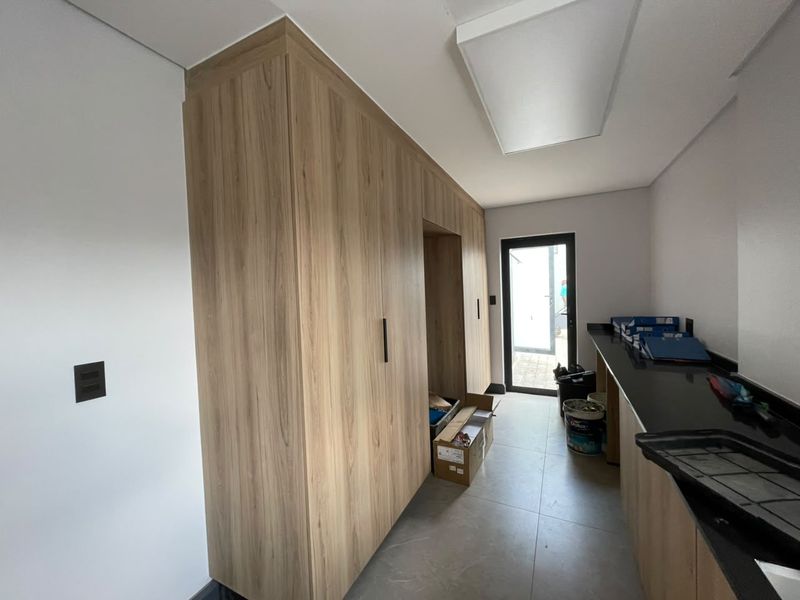 A modern scullery featuring extensive wood-grain built-in cabinetry, dark stone countertops, and tiled flooring with direct access to the exterior.