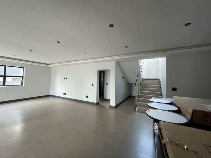 Spacious open-plan living area featuring modern tiled flooring, recessed downlights, and a contemporary staircase with a glass balustrade.