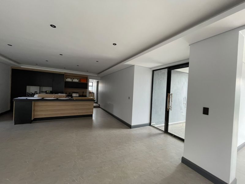 Spacious open-plan living area featuring a modern kitchen with island, neutral tiled flooring, and large sliding glass doors leading to the exterior.