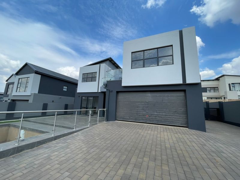 Modern double-story residential property featuring a paved driveway, double garage, and a contemporary facade with glass balustrades.
