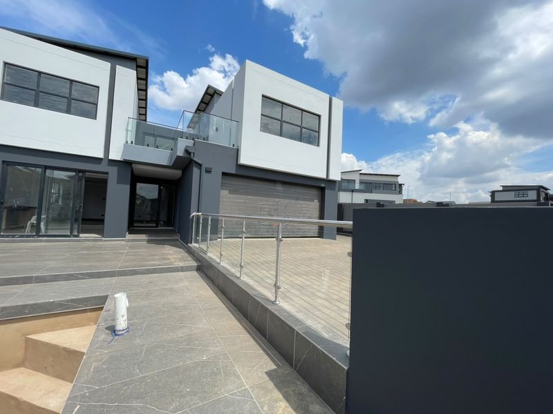Modern double-story home exterior featuring a tiled patio, glass balustrades, and a paved driveway with an integrated garage.
