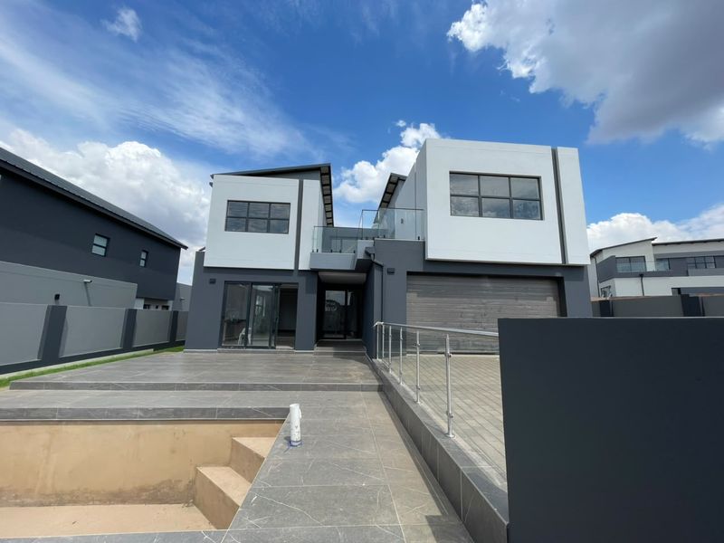 Modern double-storey residence featuring a tiled patio, glass balustrades, and an unfinished swimming pool, showcasing contemporary architectural design and clean lines.