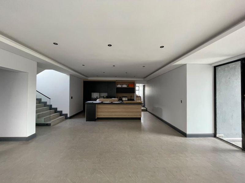 Spacious open-plan living area featuring a modern kitchen island, sleek cabinetry, recessed lighting, and a contemporary staircase with glass balustrades.