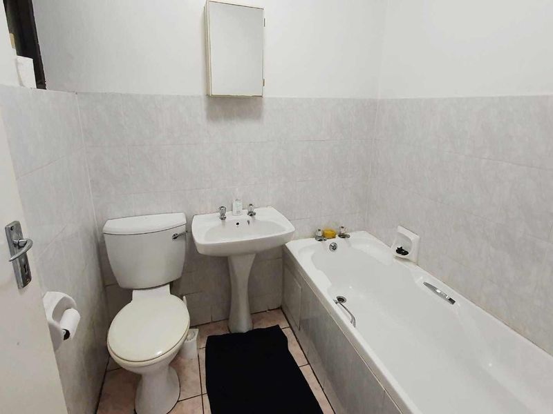 A functional bathroom featuring a pedestal basin, standard toilet, and bathtub with tiled wall finishes and a wall-mounted medicine cabinet.
