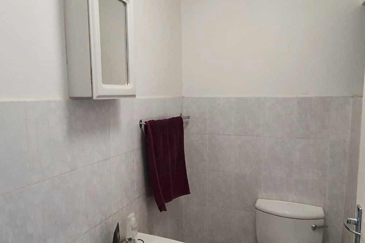 A compact bathroom featuring a wall-mounted medicine cabinet, ceramic washbasin, and standard toilet with partial wall tiling.